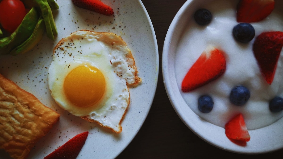 a white plate topped with a fried egg next to a bowl of fruit